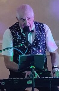 Chris in a fancy, music-themed waistcoat, playing his keyboard